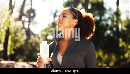 Femme heureuse, pensée et forêt avec bouteille d'eau pour la randonnée, l'hydratation ou la durabilité naturelle. Femme, randonneur ou coureur avec liquide minéral Banque D'Images
