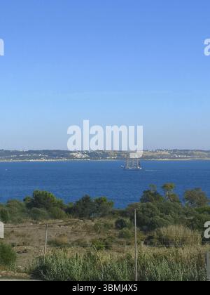 Vue panoramique d'un grand voilier naviguant sur le Tage près de Lisbonne, Portugal, avec de la verdure au premier plan et un ciel bleu clair. Banque D'Images