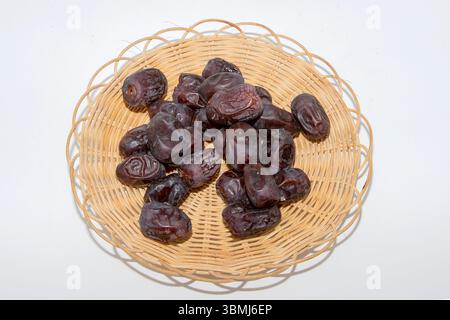 Dattes sucrées séchées dans un panier en osier sur fond blanc. Collation saine, dessert naturel et concept d'aliments biologiques. Banque D'Images