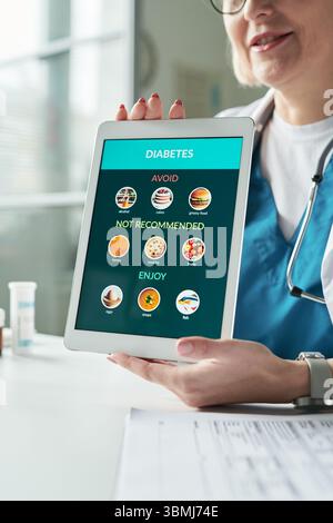 Médecin féminin caucasien d'âge moyen tenant un comprimé numérique affichant des recommandations diététiques de diabète lors de la consultation avec le patient en arrêt médical Banque D'Images
