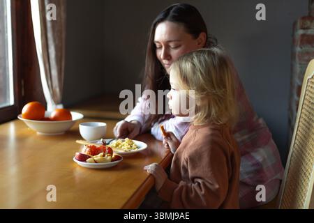 une femme et un garçon prennent le petit déjeuner à une table devant une fenêtre Banque D'Images