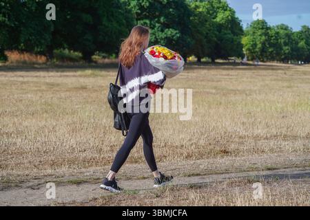 Londres, Royaume-Uni. 27 juin 2025. Une femme marche un bouquet de fleurs dans le soleil matinal lumineux sur Wimbledon Common. Une alerte météorologique orange est émise dans toute l'Angleterre à l'approche d'une deuxième vague de chaleur estivale, les températures devraient monter à 34 degrés celsius d'ici lundi. Amer Ghazzal/Alamy Live News Banque D'Images