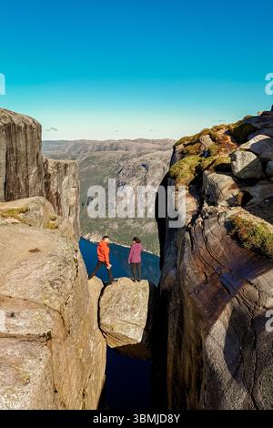 Deux aventuriers se tiennent sur une formation rocheuse au-dessus d'un fjord profond, entouré par la nature sauvage norvégienne à couper le souffle. Kjeragbolten Lysefjord, Norvège Banque D'Images