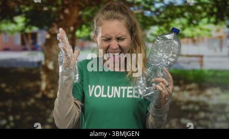 Une femme tenant une bouteille usée semble dégoûtée dans le parc car un bénévole portant des gants ramasse le plastique pendant le nettoyage des poubelles pour soutenir l'environnement. Banque D'Images