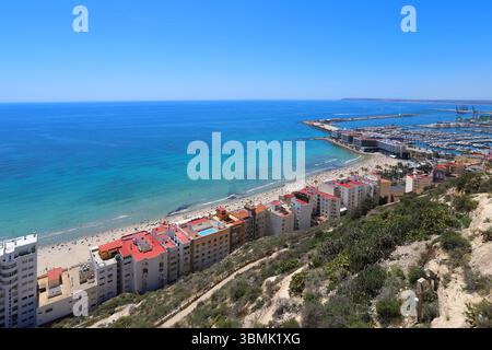 Vue sur la côte de la plage de Postiguet à Alicante avec mer bleue, hôtels modernes, palmiers et promenade en bord de mer. Banque D'Images
