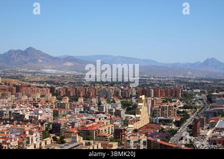 Vue sur la côte de la plage de Postiguet à Alicante avec mer bleue, hôtels modernes, palmiers et promenade en bord de mer. Banque D'Images
