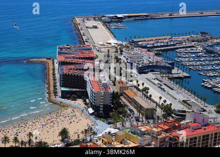 Vue sur la côte de la plage de Postiguet à Alicante avec mer bleue, hôtels modernes, palmiers et promenade en bord de mer. Banque D'Images