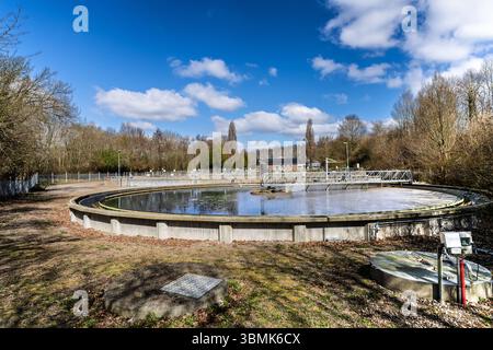 Station moderne de traitement des eaux usées avec un grand bassin rond dans un paysage rural sous un ciel bleu. Banque D'Images