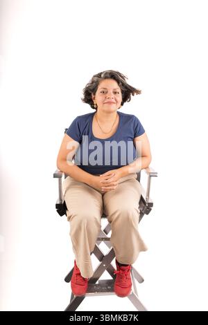 Une femme est assise sur une chaise, les bras croisés. Elle porte une chemise bleue et un pantalon bronzé Banque D'Images