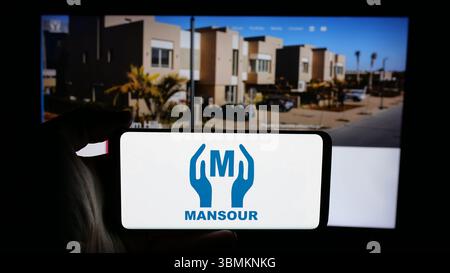 Stuttgart, Allemagne - 05-02-2025 : personne tenant un téléphone portable avec le logo de la société égyptienne Mansour Group sur l'écran en face de la page web. Banque D'Images