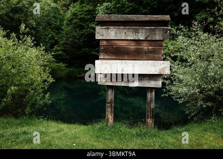 Panneau en bois altéré sur pilotis se tient près d'une rivière calme et verte entourée de forêt. Une scène d'une réserve naturelle tranquille. Copier l'espace pour les voyages et Banque D'Images