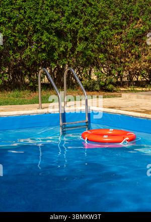 La bouée de sauvetage flotte dans la piscine bleue, symbolisant la sécurité aquatique et la détente estivale. Idéal pour les voyages, les services de sauvetage et la conception de vacances au bord de la piscine Banque D'Images