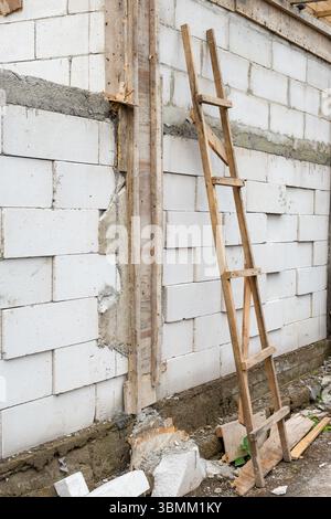 Échelle en bois appuyée contre un mur. L'échelle est appuyée contre un mur fait de briques. Les briques sont blanches et l'échelle est brune Banque D'Images