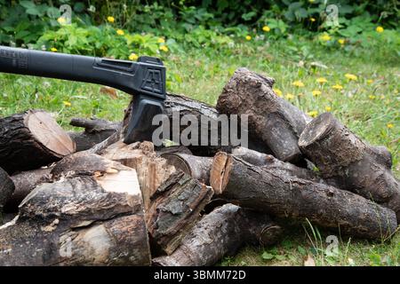 Scène extérieure avec une hache intégrée dans un bloc de coupe à côté d'un tas de bûches, suggérant une vie rustique, la préparation du bois de chauffage, ou le travail dans les bois. Banque D'Images