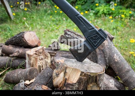 Scène extérieure avec une hache intégrée dans un bloc de coupe à côté d'un tas de bûches, suggérant une vie rustique, la préparation du bois de chauffage, ou le travail dans les bois. Banque D'Images