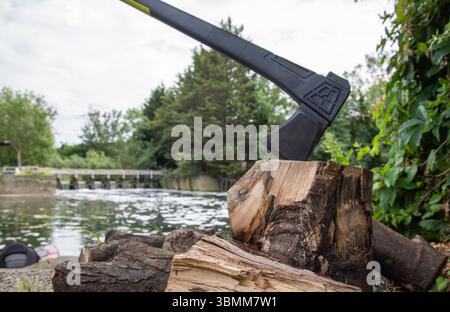 Scène extérieure avec une hache intégrée dans un bloc de coupe à côté d'un tas de bûches, suggérant une vie rustique, la préparation du bois de chauffage, ou le travail dans les bois. Banque D'Images