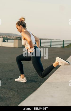 Une femme athlétique effectue un squat fractionné bulgare, un type de fente sur une jambe, pendant son entraînement de musculation en plein air. Banque D'Images