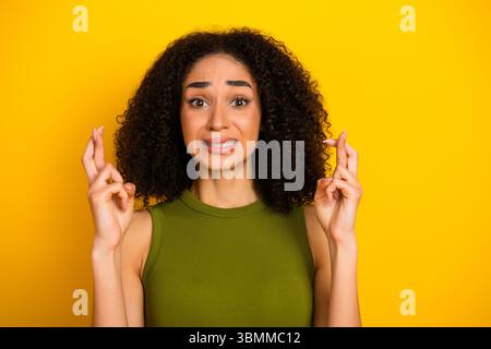 Jeune femme pleine d'espoir croisant les doigts sur fond jaune pour la positivité et la chance, la mode décontractée et le style confiant Banque D'Images