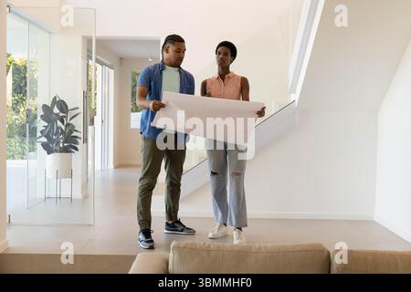Couple examinant un grand plan dans un salon moderne, avec canapé neutre et plante en pot Banque D'Images
