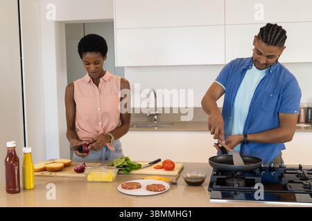 Hacher l'oignon rouge et frire les galettes, cuisiner un couple varié sur l'îlot de cuisine avec planche à découper Banque D'Images