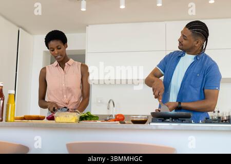Couple diversifié cuisiner ensemble à la maison îlot de cuisine, avec planche à découper et ingrédients frais Banque D'Images