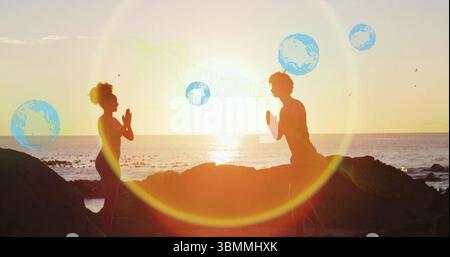 Couple pratiquant dans des vêtements d'action tenant la pose de prière sur l'affleurement rocheux au coucher du soleil, avec l'océan en toile de fond Banque D'Images