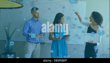 Équipe de collaboration esquissant des diagrammes sur tableau blanc au bureau avec ordinateur portable et icônes de données Banque D'Images