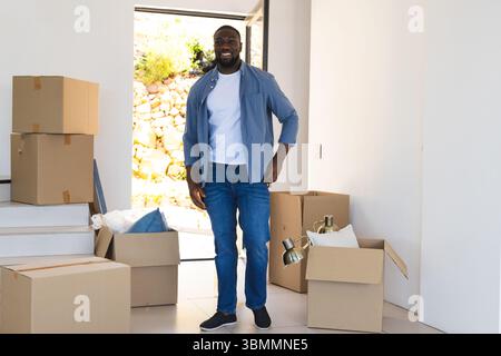 Homme afro-américain adulte debout dans l'entrée au milieu de boîtes mobiles triant les oreillers lampe bulle enveloppant Banque D'Images