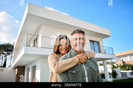 Heureux souriant couple vieux nouveaux propriétaires de maison debout à l'extérieur de la maison. Banque D'Images