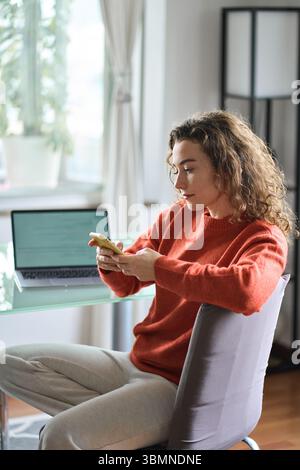 Jeune femme qui utilise un téléphone portable tout en travaillant à la maison. Banque D'Images