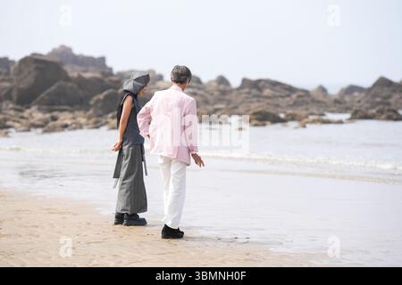 En juin 2025, un homme et une femme coréens dans la cinquantaine se tiennent debout et parlent à côté du rivage accidenté rempli de rochers déchiquetés et de s'écraser Banque D'Images