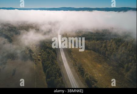 Promenade panoramique à travers un paysage couvert de brouillard à la lumière du petit matin, mettant en valeur une autoroute sinueuse et un terrain luxuriant Banque D'Images
