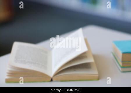 Le livre de poche ouvert de conception plate repose sur une table avec une pile de livres colorés, une étagère floue Banque D'Images