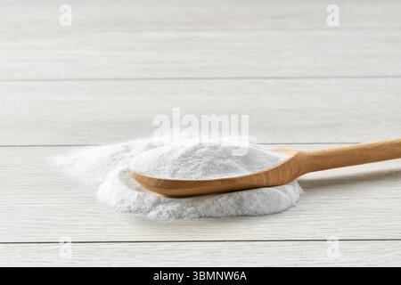 Bicarbonate de soude dans une cuillère en bois sur une table en bois blanc. Banque D'Images
