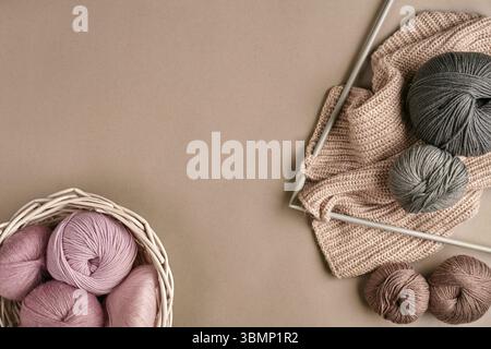 Boules de fil de laine mérinos, tricot sur aiguilles à tricoter sur une surface de couleur beige. Rose, blanc et gris de la balle de thread dans le panier. Vue d'en haut. La vie encore. C Banque D'Images