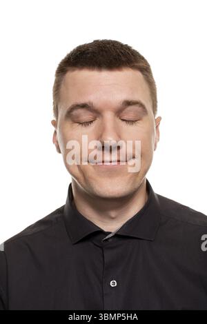 Huebscher junger Mann im schwarzen Hemd schneidet Grimassen, waehrend er isoliert auf einem weissen Hintergrund steht Banque D'Images