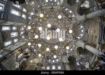 Vue en bas angle d'un grand lustre suspendu au plafond d'une mosquée, éclairant le dôme et l'architecture environnante Banque D'Images