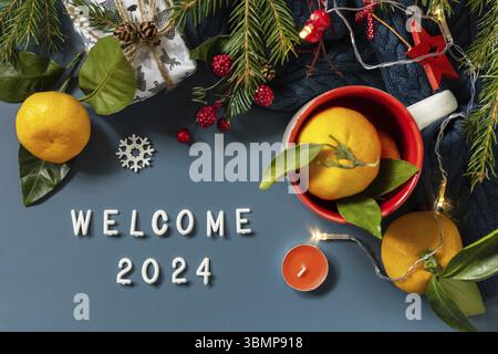 Texte de bienvenue 2024. Composition hivernale avec branches de sapin, présentes, cônes et mandarines sur fond bleu. Ambiance hivernale chaleureuse. Vue de dessus Banque D'Images