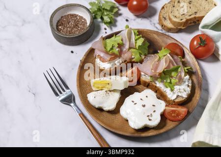 Petit-déjeuner ou brunch de Pâques. Délicieux petit déjeuner ou en-cas - œufs pochés et fromage à la crème pain de seigle complet, prosciutto, arugula sur un t de marbre Banque D'Images
