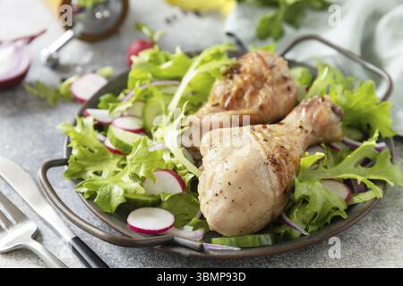 Saine alimentation propre. Viande et salade fraîche. Des pilons de poulet cuits et une salade végétalienne verte faite à partir d'un de feuilles vertes et de légumes de printemps sur un s. Banque D'Images