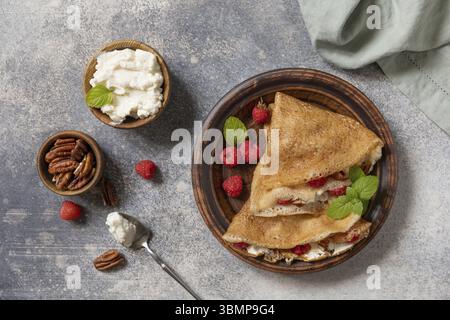 Savoureuses crêpes sucrées maison farcies aux framboises, aux noix de pécan et au fromage à la crème sur un fond de pierre grise. Crêpes fines, blini. Dessert sucré. Vue avant Banque D'Images