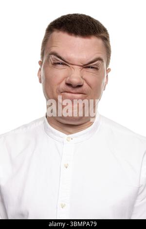 Charmanter huebscher junger Mann im weissen Hemd schneidet Grimassen, waehrend er isoliert auf einem weissen Hintergrund steht Banque D'Images