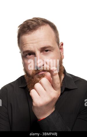 Portrait d'un jeune homme roux, poêlé, avec une barbe dans une chemise noire, pointant vers quelqu'un et regardant réfléchi, isolé sur un fond blanc Banque D'Images