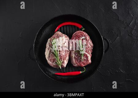 Les viandes fraîches. Filet de boeuf steak et deux steaks de bœuf persillé sur poêle à frire et conseil avec assaisonnement, fond noir vue d'en haut. La vie encore. Banque D'Images