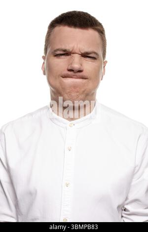 Charmanter huebscher junger Mann im weissen Hemd schneidet Grimassen, waehrend er isoliert auf einem weissen Hintergrund steht Banque D'Images