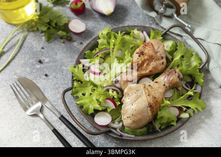 Saine alimentation propre. Viande et salade fraîche. Des pilons de poulet cuits et une salade végétalienne verte faite à partir d'un de feuilles vertes et de légumes de printemps sur un s. Banque D'Images