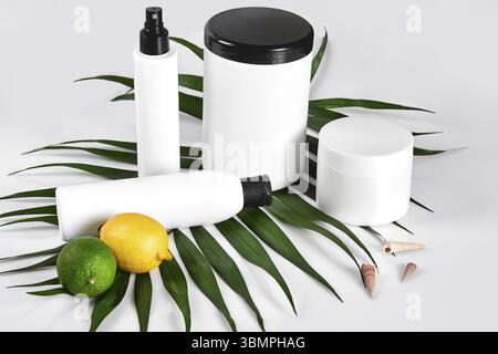 Cosmétiques naturels pour home spa. Vue de dessus des bouteilles de shampoing, crème, masque à l'huile essentielle de citron vert frais, fruits, vert feuille décor, fond blanc. Its Banque D'Images
