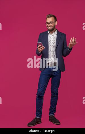 Studio shot of attractive brunette business man avec des lunettes, en chemise décontractée et élégante veste noire à parler au téléphone cellulaire et souriant. Pi isolé Banque D'Images