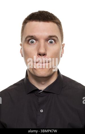 Huebscher junger Mann im schwarzen Hemd schneidet Grimassen, waehrend er isoliert auf einem weissen Hintergrund steht Banque D'Images