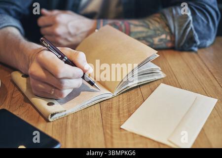 Main d'homme avec stylo écriture sur cahier sur une table en bois. Homme travaillant au café. Gros plan Banque D'Images